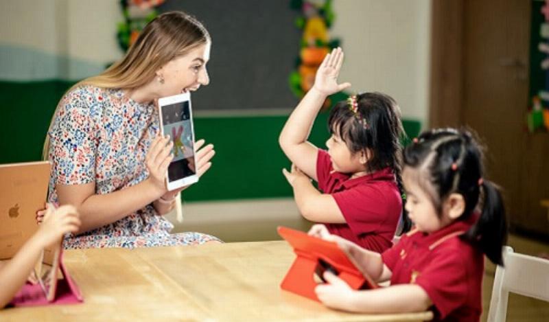 Một phụ huynh và con cùng ngồi làm bài tập nhìn hình điền từ trên bàn học, thể hiện sự đồng hành.