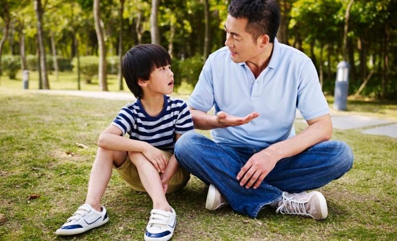 Hình ảnh cha mẹ đang ngồi ngang tầm mắt và lắng nghe con nói một cách chăm chú, minh họa kỹ năng lắng nghe chủ động trong nội dung nói với con