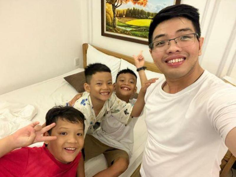 Một người lớn và một đứa trẻ đang cùng nhau dọn dẹp nhà cửa, người lớn đang lau bàn còn đứa trẻ đang xếp đồ chơi vào hộp, cả hai đều mỉm cười hợp tác.