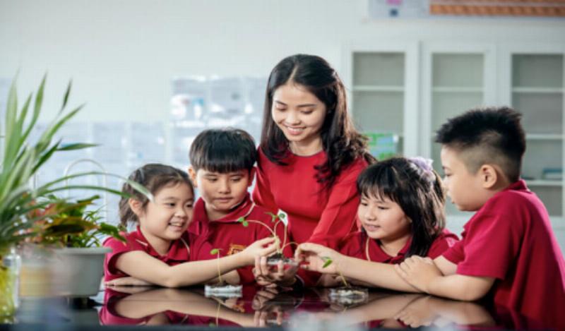 Một em bé đang ngồi trên sàn nhà với sách vở, "dạy học" cho một vài bạn thú nhồi bông về một chủ đề học tập.