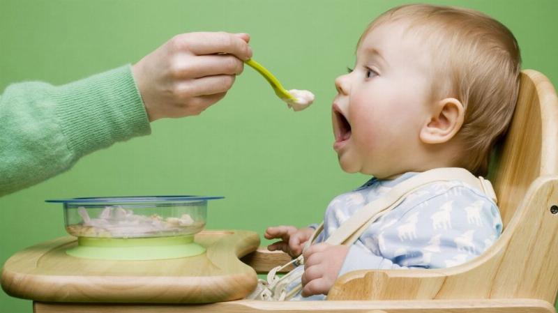 Hình ảnh bé ngồi trong ghế ăn dặm vui vẻ với bát bột đầu tiên